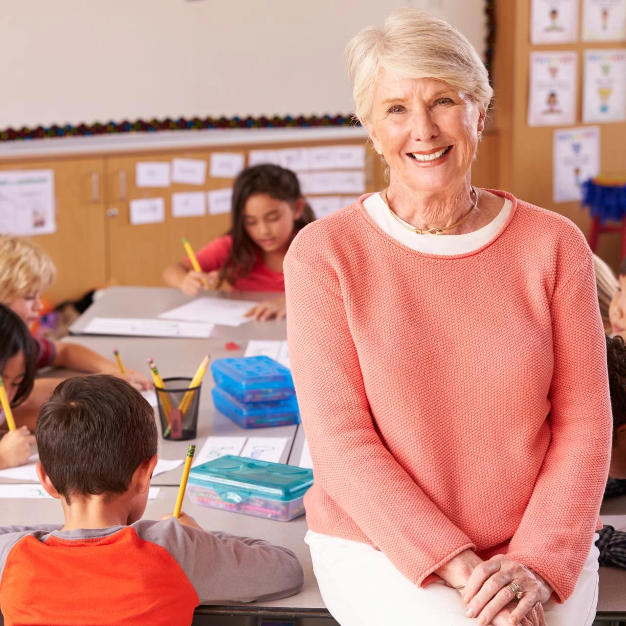 Older female teacher smiling next to her students working