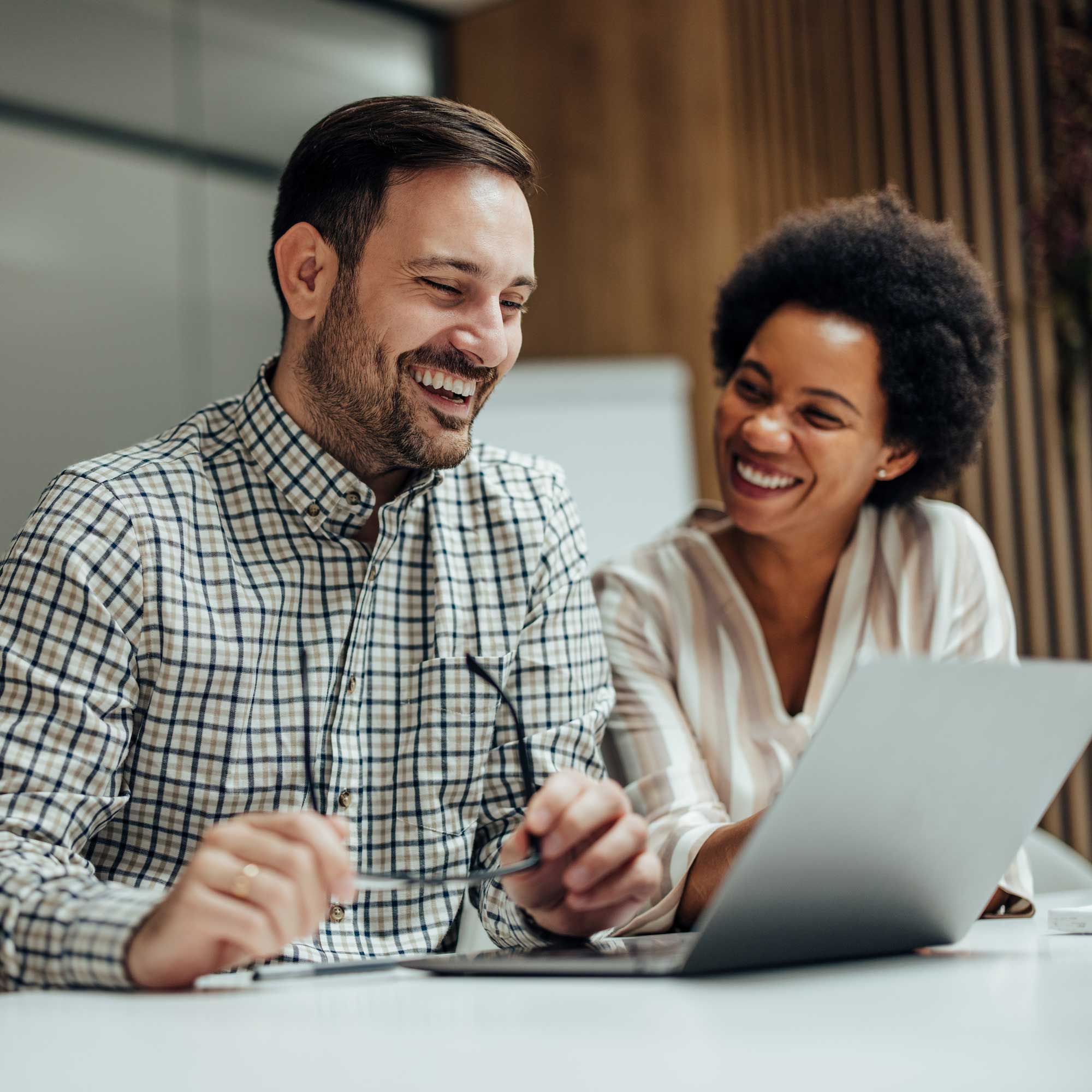 Two school employees smiling and happy looking at their laptop together